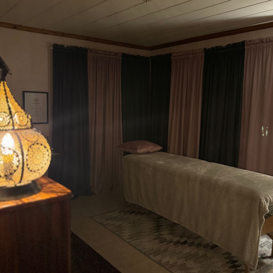 Behandlingsrum med massagebänk, dämpad belysning och varma textilier som skapar en rofylld atmosfär hos Björkbackas ljus & dekor i Karbenning, Norbergs kommun. Här utförs regndroppsmassage och neuro auricular technique.