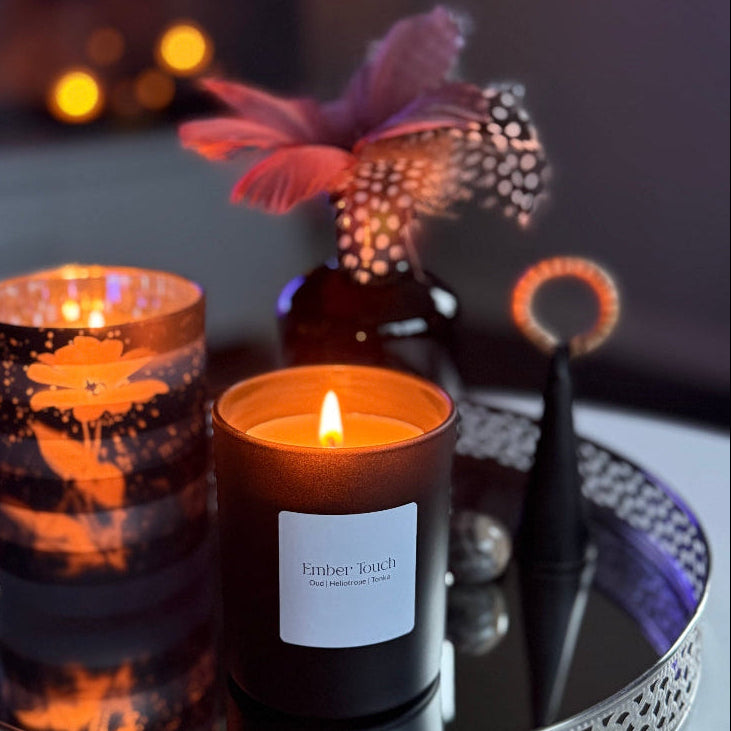 Doftljuset Ember Touch i mattsvart glas från Björkbackas ljus & dekor, brinner på en dekorativ spegelbricka med mjuk kvällsbelysning.