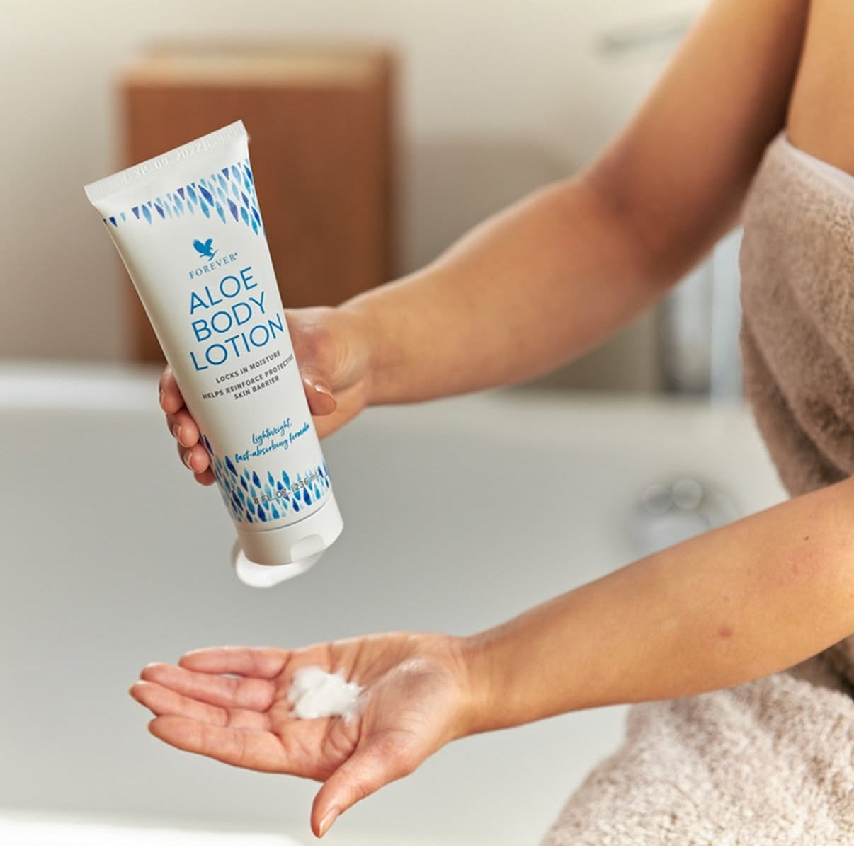 Forever Aloe Body Lotion i handen på en person vid badkar, redo att appliceras.