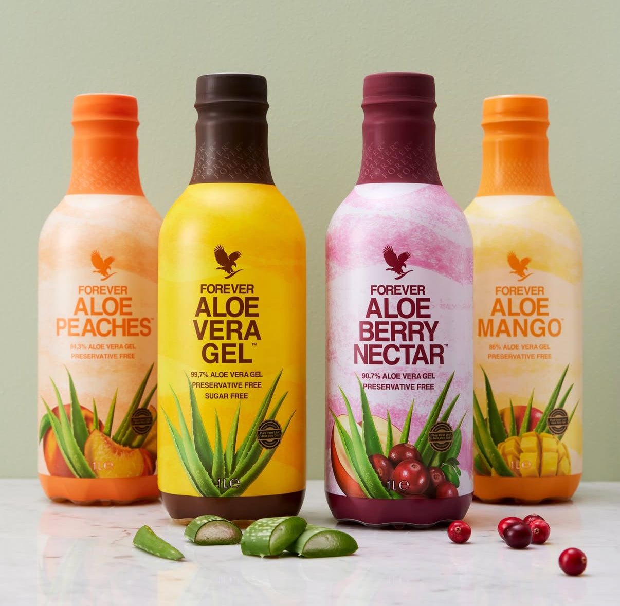 Forever Aloe-drycker i flera smaker uppställda på ljus bakgrund med aloe vera-gelé och bär i förgrunden.