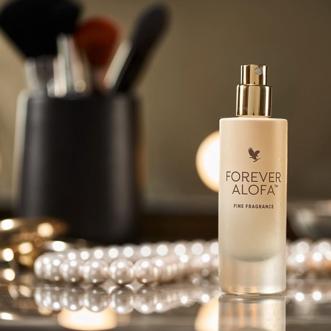 Forever Alofa Fine Fragrance flaska på sminkbord med sminkborstar och pärlhalsband i bakgrunden.