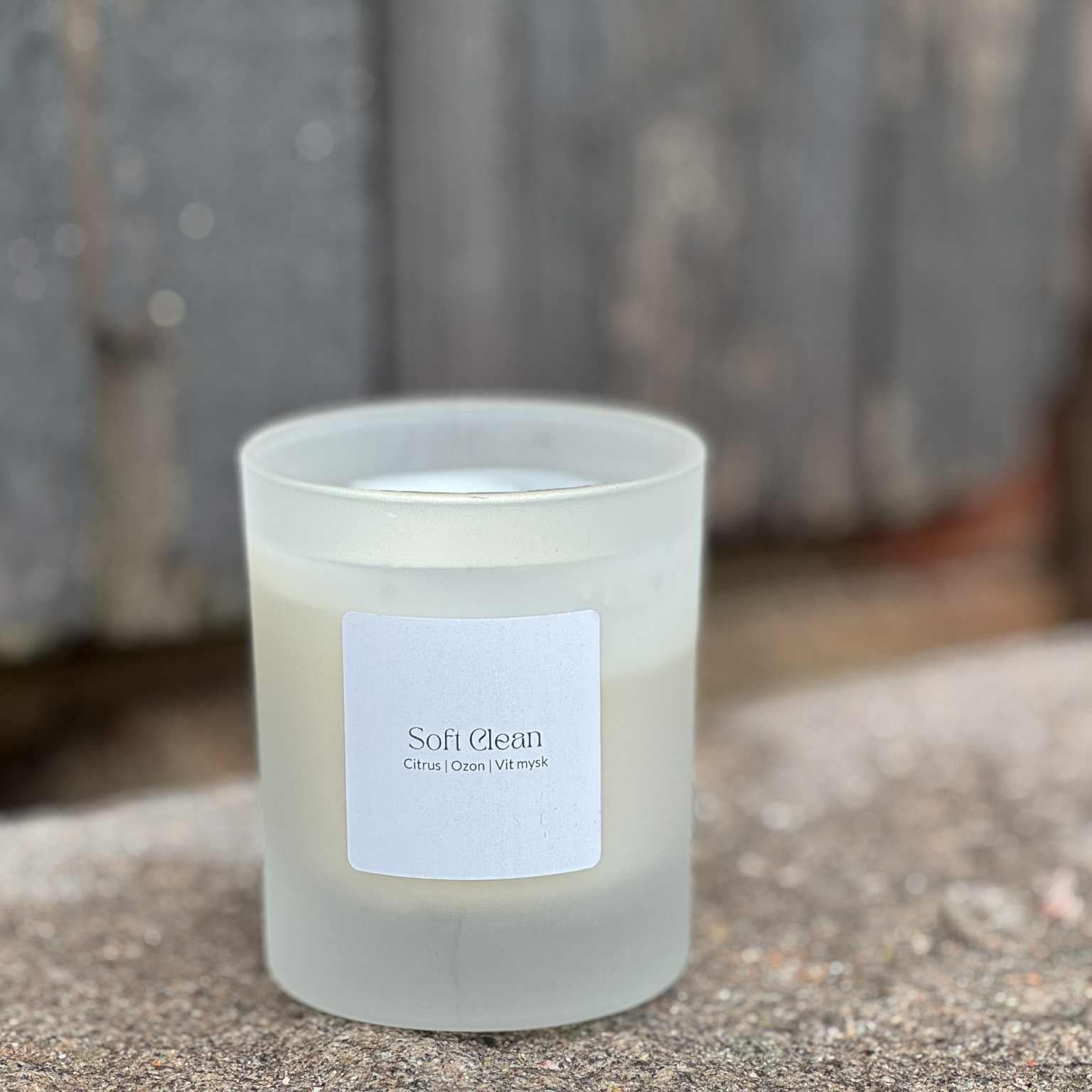 Doftljuset Soft Clean i frostat vitt glas placerat på sten mot ljusgrå träbakgrund.